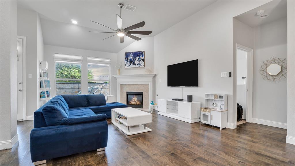 Living room featuring vaulted ceilings, wood-finish flooring, a fireplace with a decorative mantel, and a multi-blade ceiling fan Living room featuring vaulted ceilings, wood-finish flooring, a fireplace with a decorative mantel, and a multi-blade ceiling fan
