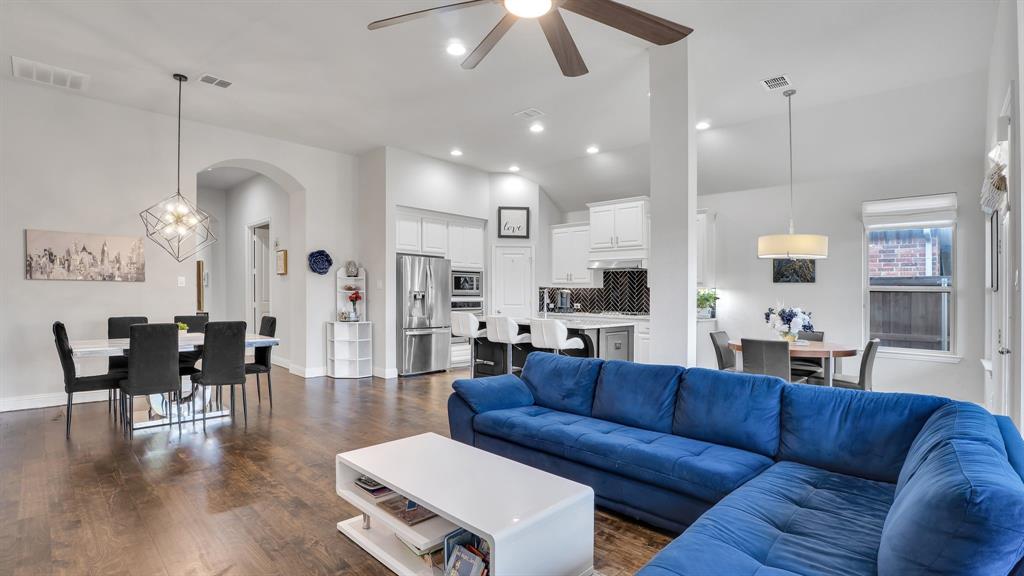 Open-concept interior featuring wood-finish flooring, vaulted ceilings, white cabinetry, a kitchen island with seating, and geometric pendant lighting Open-concept interior featuring wood-finish flooring, vaulted ceilings, white cabinetry, a kitchen island with seating, and geometric pendant lighting