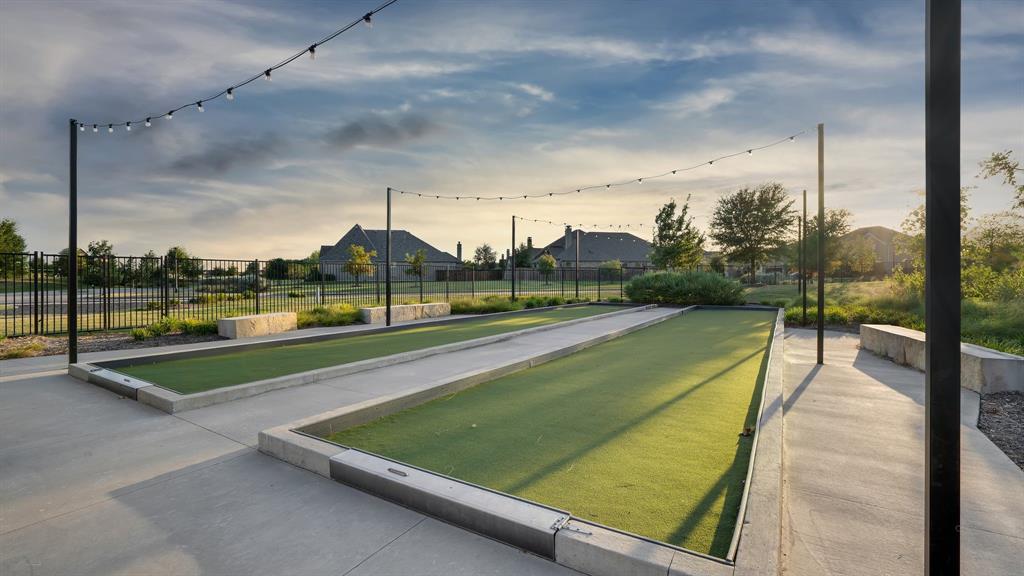 Dual bocce ball courts featuring synthetic turf, concrete borders, stone block seating, and overhead string lighting