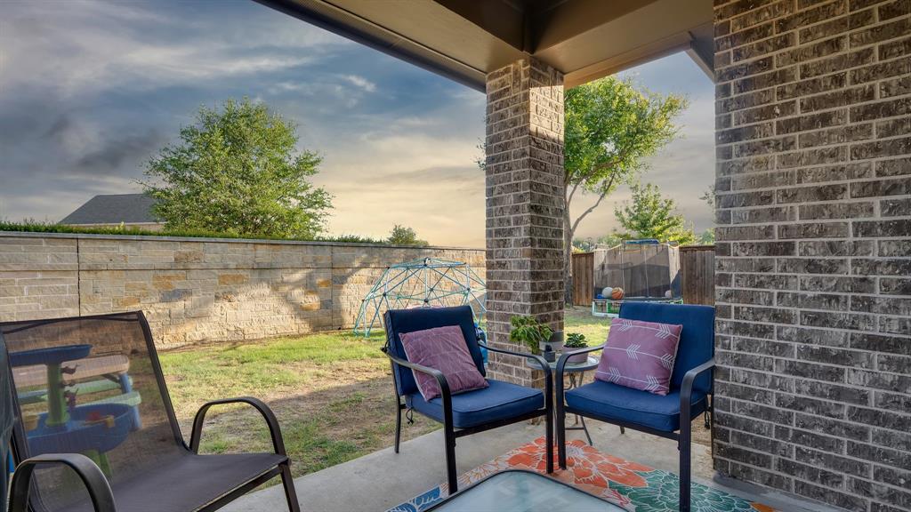 Covered patio featuring a concrete floor and brick structural pillar, opening to a private backyard enclosed by a stone perimeter wall