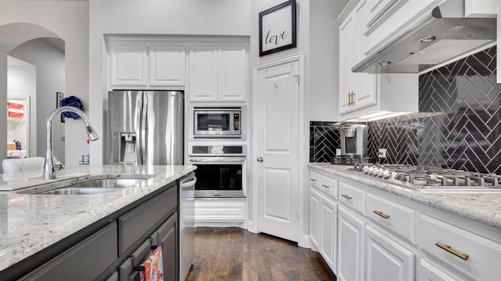 Kitchen featuring white shaker-style cabinetry, stone countertops, stainless steel appliances, built-in wall oven and microwave, and black herringbone-patterned tile backsplash Kitchen featuring white shaker-style cabinetry, stone countertops, stainless steel appliances, built-in wall oven and microwave, and black herringbone-patterned tile backsplash