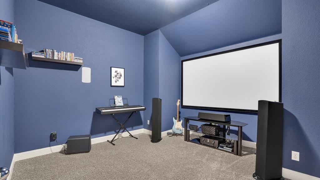 Dedicated media room featuring a wall-mounted projector screen, vaulted ceilings, and wall-mounted shelving