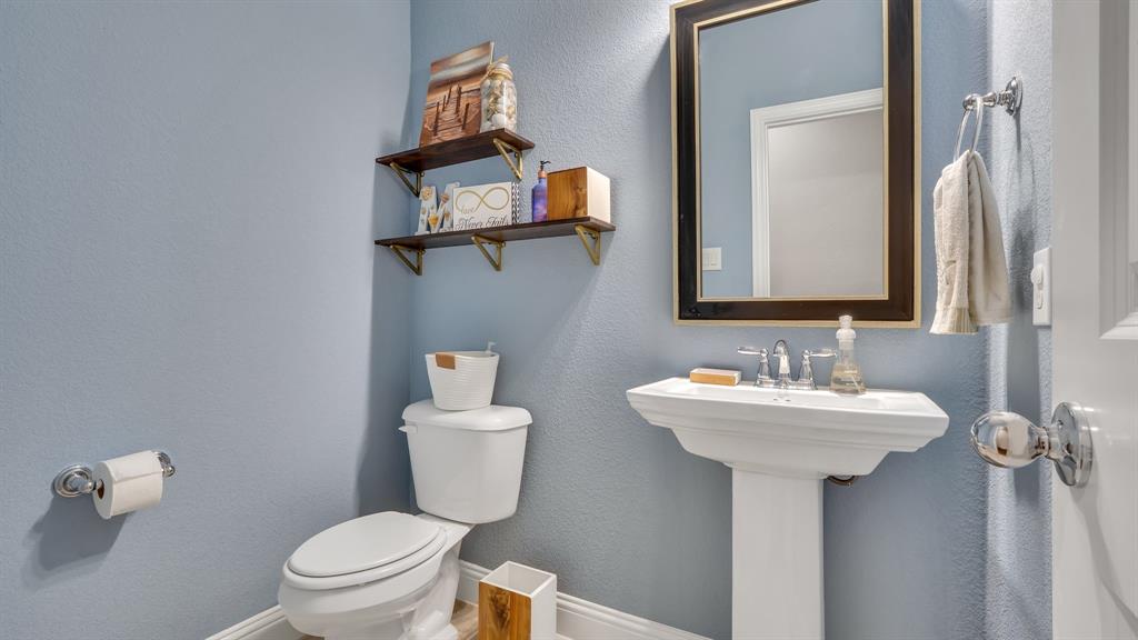 Pedestal sink with polished chrome widespread faucet, framed wall mirror, and two wall-mounted wooden shelves with metal brackets