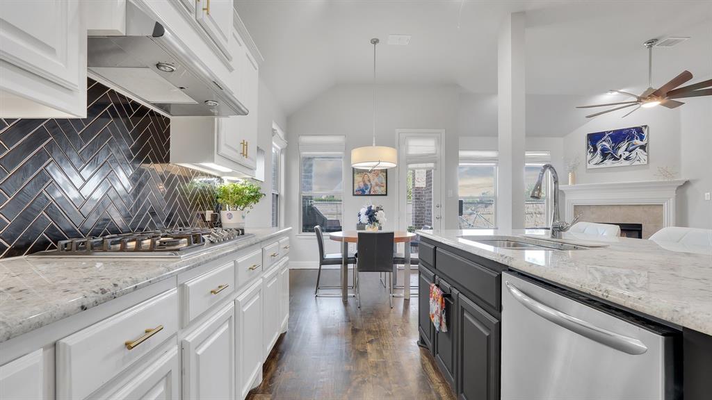 Kitchen featuring white shaker-style cabinetry, black herringbone tile backsplash, stone-finish countertops, stainless steel appliances, and wood-finish flooring Kitchen featuring white shaker-style cabinetry, black herringbone tile backsplash, stone-finish countertops, stainless steel appliances, and wood-finish flooring