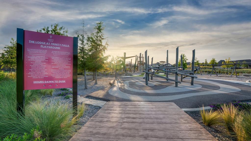 Recreational area featuring modern climbing structures, patterned poured-surface flooring, a wood-finish pathway, and native landscaping