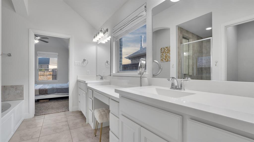 Bathroom featuring a dual-sink vanity with white cabinetry and solid-surface countertops, large wall-mounted mirrors, tile flooring, and a soaking tub