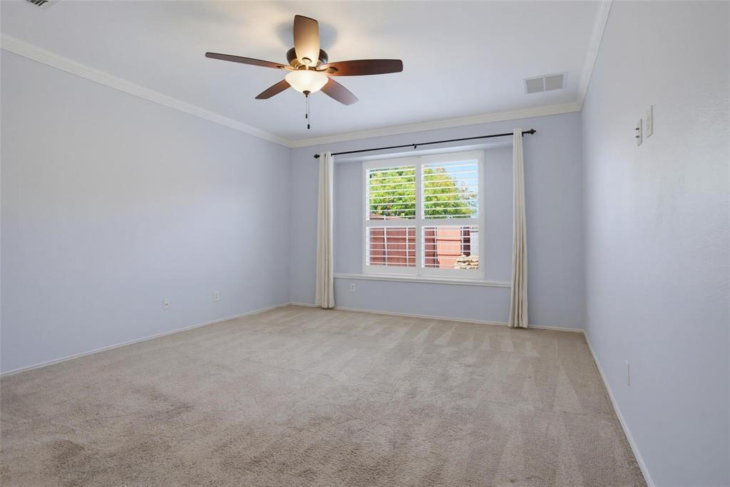 Neutral wall tones, carpeted flooring, multi-pane window with plantation shutters, crown molding, and a multi-blade ceiling fan with integrated light fixture