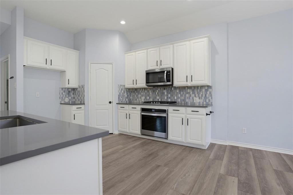 Kitchen featuring white cabinetry, solid surface countertops, a mosaic tile backsplash, stainless steel appliances, and wood-finish flooring