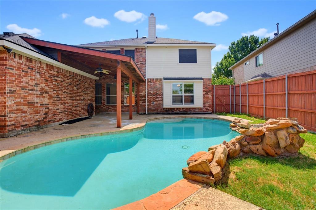 Backyard featuring an in-ground swimming pool with a stone water feature, a covered patio with wooden structural supports, brick and siding exterior, and a wood privacy fence