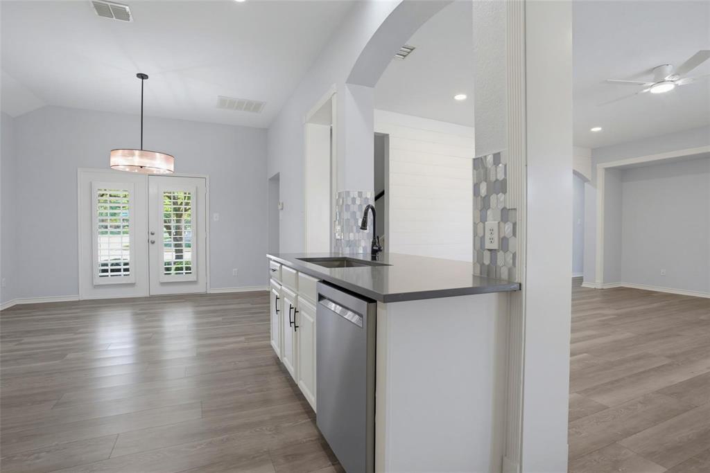 Kitchen featuring a peninsula with solid-surface countertops, stainless steel dishwasher, and a faucet with a pull-down sprayer, accented by a hexagonal tile backsplash and wood-finish flooring throughout