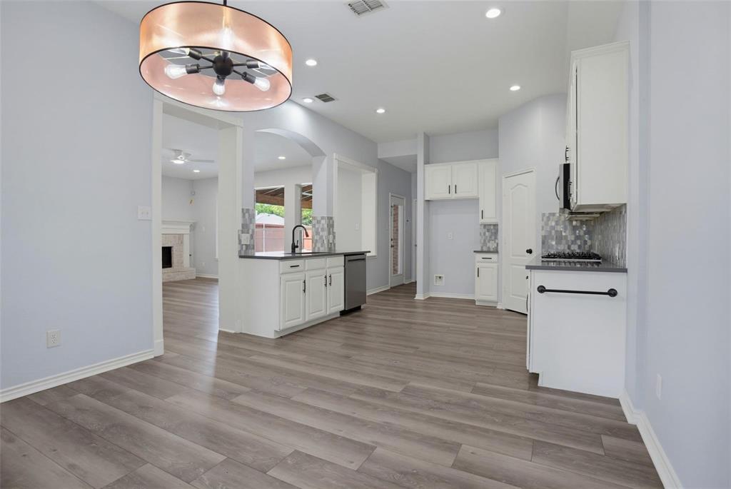 Kitchen featuring white shaker-style cabinetry, dark stone-finish countertops, mosaic tile backsplash, wood-finish flooring, and a drum-style pendant light fixture