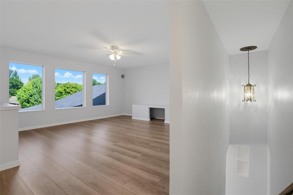 Open interior space featuring wood-finish flooring, multiple windows, a ceiling fan, a built-in desk, and a pendant light fixture Open interior space featuring wood-finish flooring, multiple windows, a ceiling fan, a built-in desk, and a pendant light fixture