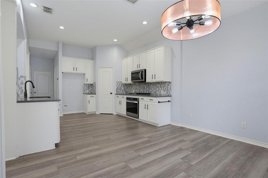 Kitchen featuring white cabinetry, wood-finish flooring, stone-style tile backsplash, built-in stainless steel appliances, and a modern drum-style pendant light fixture