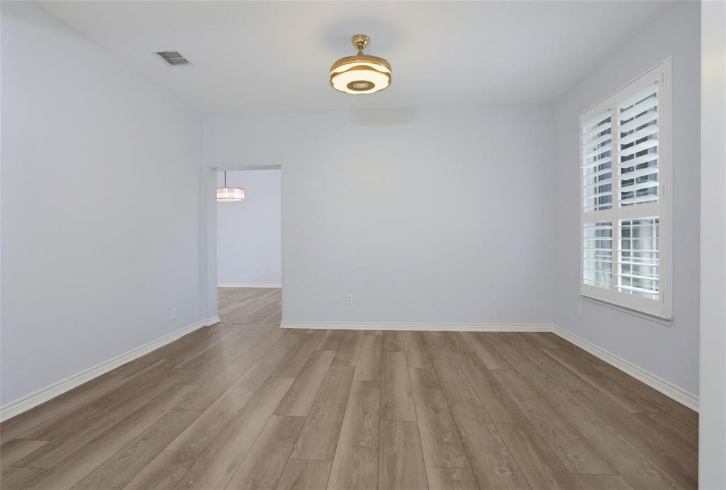 Interior space featuring wood-finish flooring, white plantation shutters, and a modern drum-style flush-mount light fixture