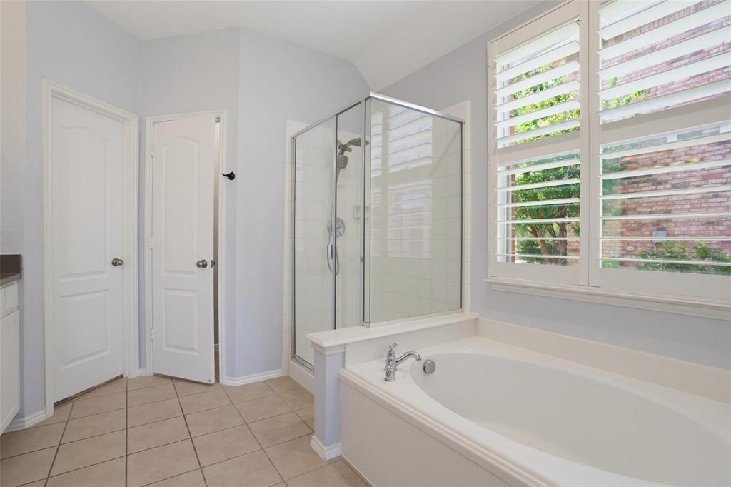 Bathroom featuring an oval soaking tub, separate glass-enclosed shower, tile flooring, and plantation shutters