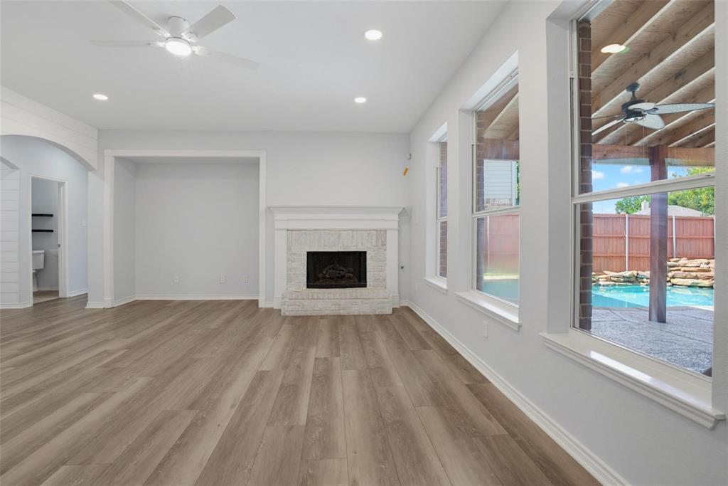 Living area featuring wood-finish flooring, a masonry fireplace with a white mantel, recessed lighting, and large windows with exterior pool and covered patio visibility