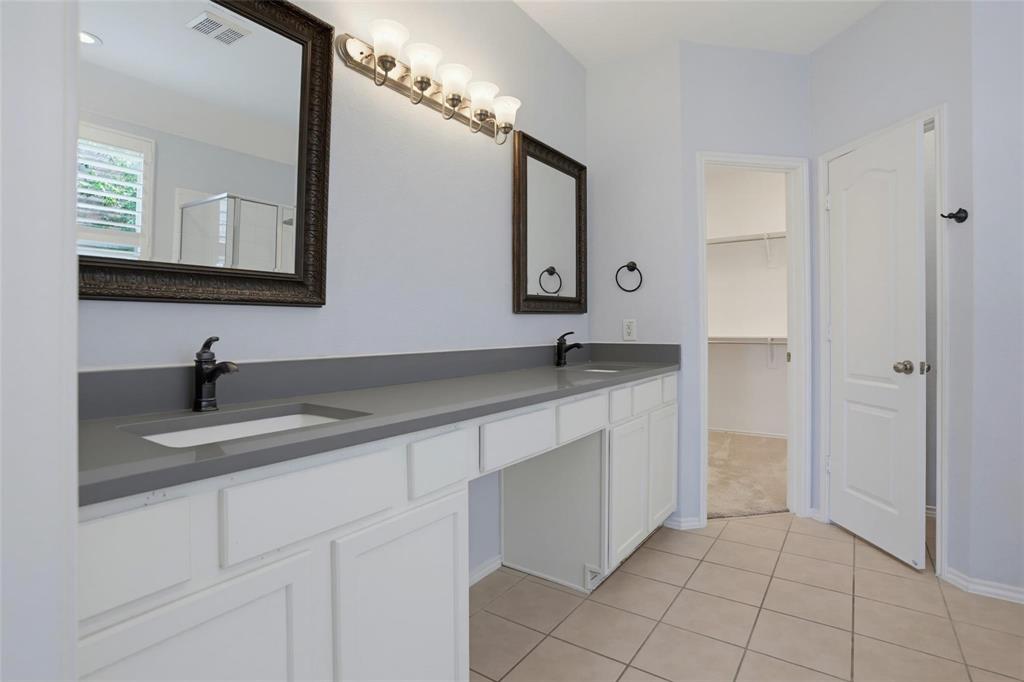 Double-vanity cabinet with white shaker-style doors, matte gray solid-surface countertop, dual under-mount sinks with dark metal faucets, and multi-light vanity fixtures