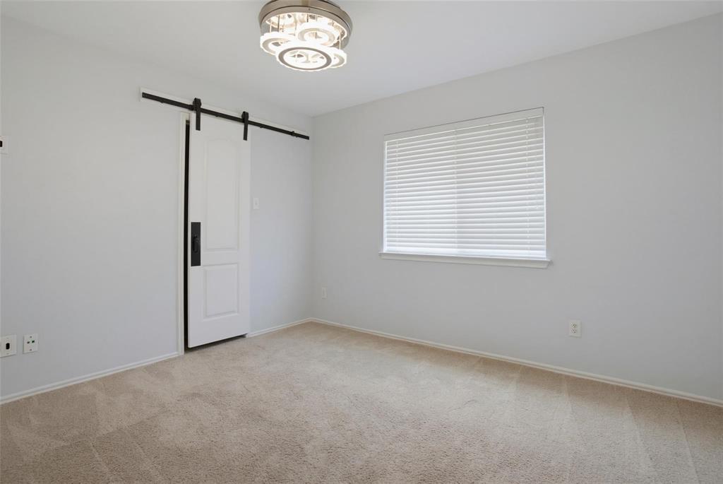 Room featuring neutral carpeting, a sliding barn-style door with matte black hardware, horizontal window blinds, and a modern circular tiered flush-mount light fixture Room featuring neutral carpeting, a sliding barn-style door with matte black hardware, horizontal window blinds, and a modern circular tiered flush-mount light fixture
