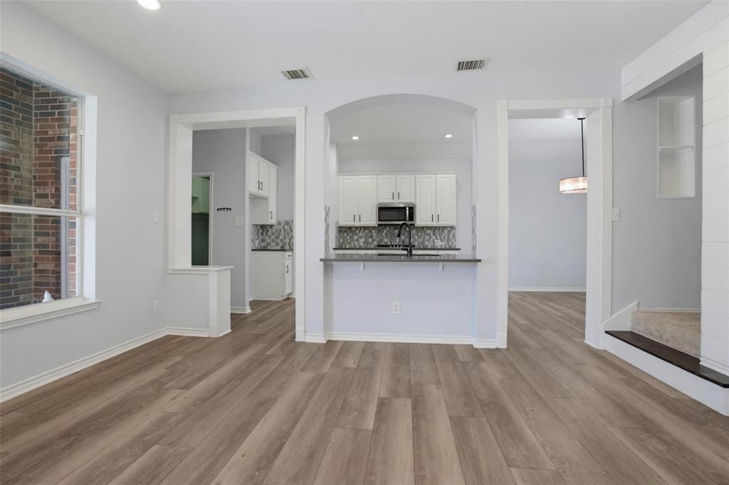 Interior space featuring wood-finish flooring, an arched kitchen entryway, white cabinetry, a breakfast bar with stone-finish countertops, and an exposed brick accent wall