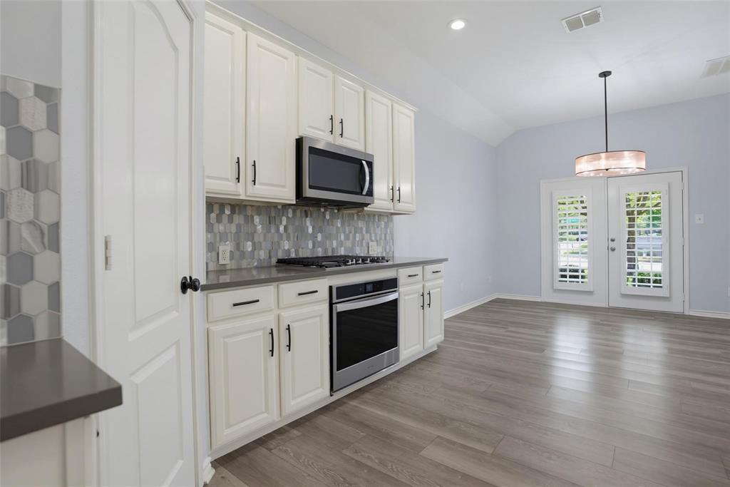Kitchen featuring white cabinetry, solid-surface countertops, a mosaic tile backsplash, stainless steel appliances, and wood-finish flooring