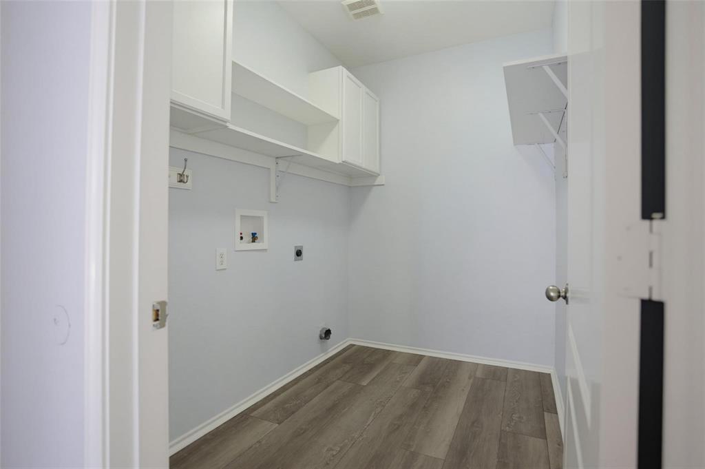 Utility room featuring wood-finish flooring, white shaker-style cabinetry, open wall shelving, and dedicated hookups for laundry appliances