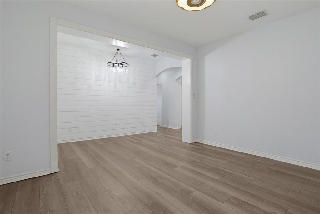 Interior space featuring wood-finish flooring, horizontal shiplap wall detailing, an overhead tiered chandelier, and arched architectural framing