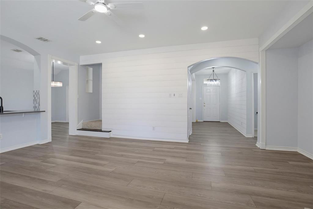 Open interior featuring wood-finish flooring, white shiplap accent wall, arched doorways, recessed lighting, and a ceiling fan with integrated light fixture