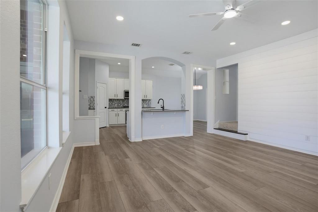 Open-concept interior featuring wood-finish flooring, shiplap wall detailing, arched architectural openings, recessed lighting, and a kitchen island with a matte black faucet