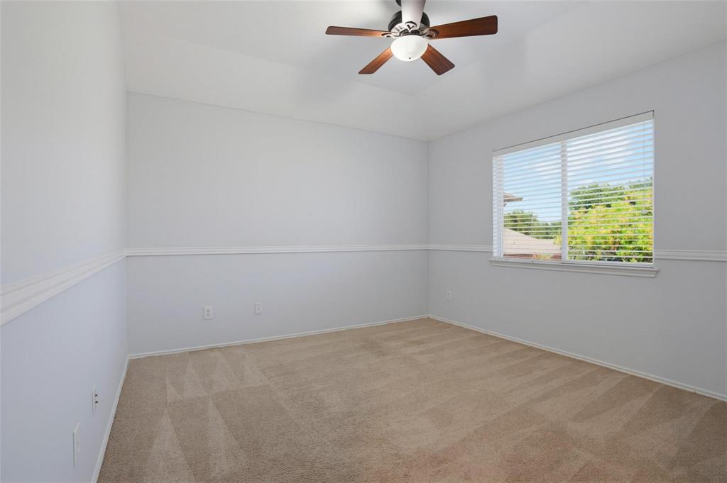 Room interior featuring neutral carpeting, a tray ceiling, ceiling fan with integrated lighting, chair rail molding, and window with blinds Room interior featuring neutral carpeting, a tray ceiling, ceiling fan with integrated lighting, chair rail molding, and window with blinds