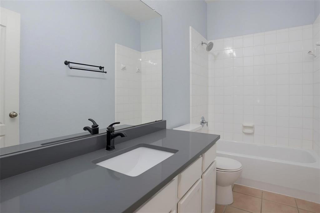 Bathroom featuring a vanity with a dark solid-surface countertop, an undermount sink, and matte black hardware, paired with a floor-to-ceiling mirror, a porcelain-tiled tub surround, and ceramic tile flooring