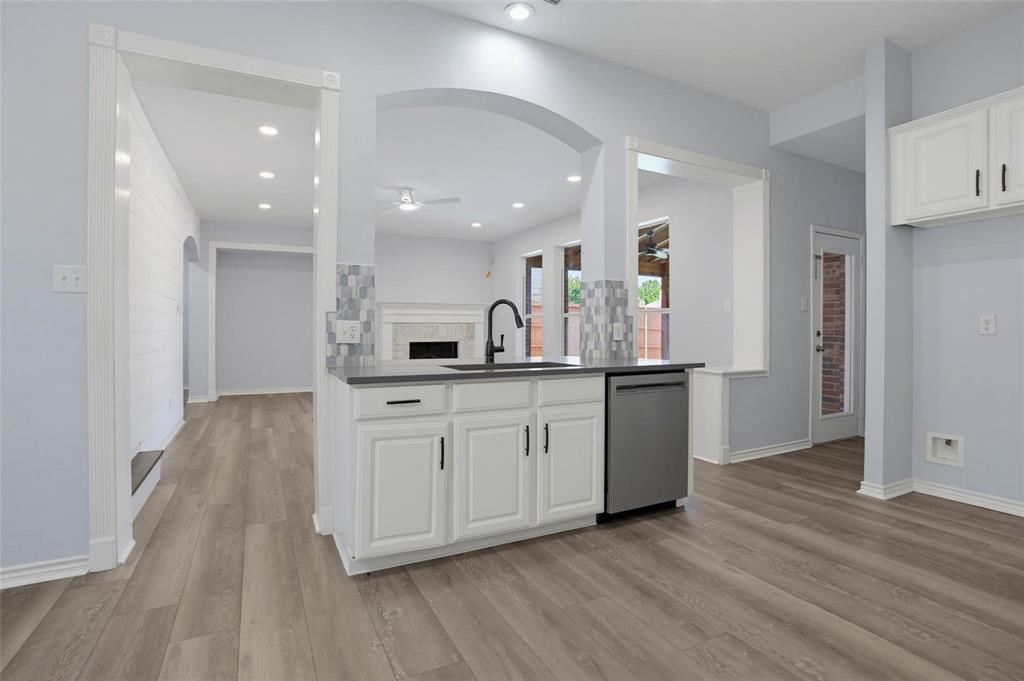 Kitchen island featuring a stone-surface countertop, under-mount sink with a matte black pull-down faucet, white shaker-style cabinetry, stainless steel dishwasher, and mosaic tile backsplash Kitchen island featuring a stone-surface countertop, under-mount sink with a matte black pull-down faucet, white shaker-style cabinetry, stainless steel dishwasher, and mosaic tile backsplash