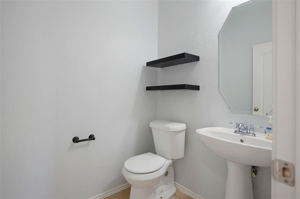 Powder room featuring a pedestal sink, wall-mounted octagonal mirror, dual black floating shelves, and a matte black hardware finish