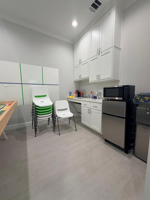 Floor-to-ceiling white cabinetry, wood-finish flooring, integrated sink with stone countertop, and crisp neutral wall finish