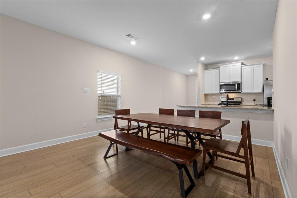 Open-concept area featuring wood-finish flooring, recessed lighting, and a kitchen equipped with white cabinetry, stone-finish countertops, and stainless steel appliances