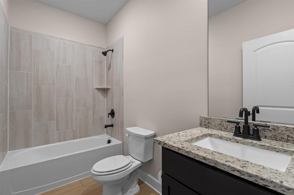 Bathroom featuring a dark wood vanity with stone-style countertop, undermount sink, matte black fixtures, and a tub-shower combination with vertical tile surround
