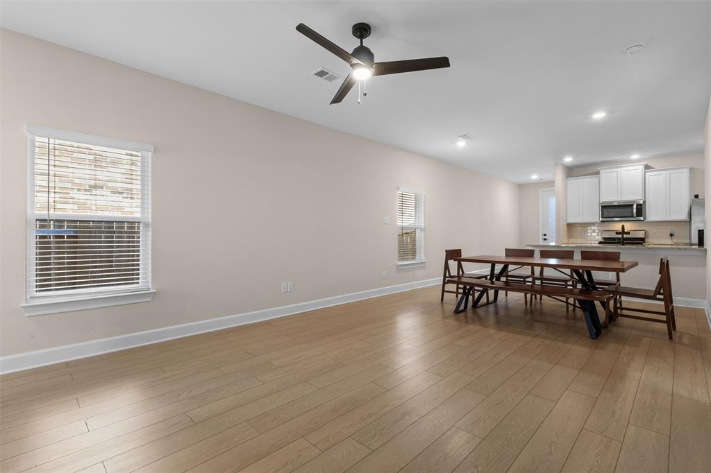 Open-concept interior featuring wood-finish flooring, recessed lighting, a modern ceiling fan, and white kitchen cabinetry with a breakfast bar