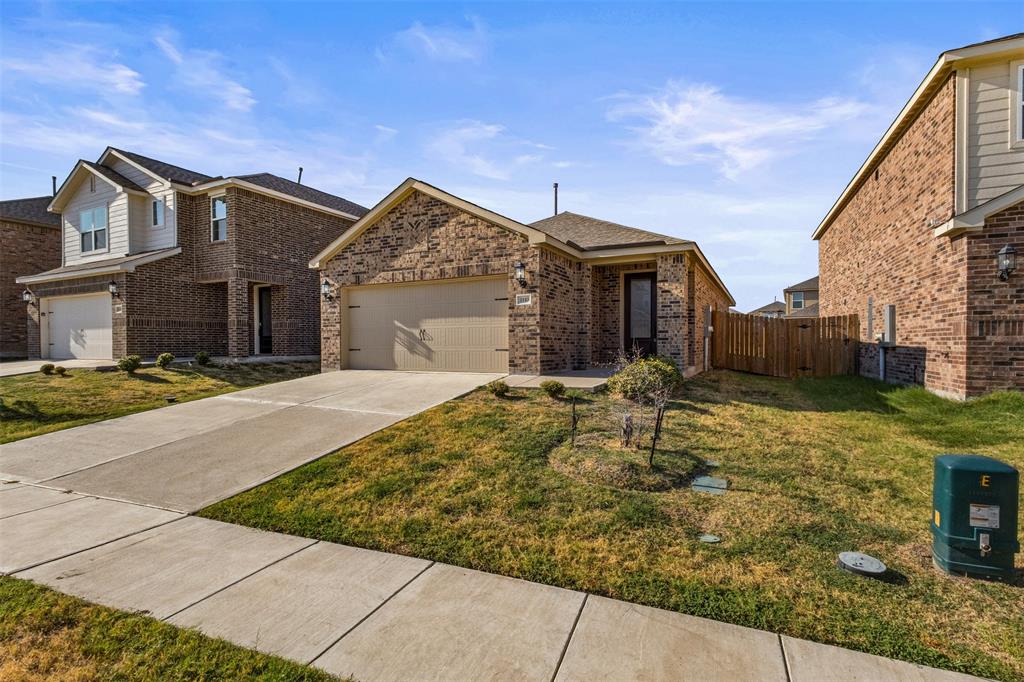 Single-story brick exterior featuring a covered front entryway, attached two-car garage, concrete driveway, and side wood privacy fencing
