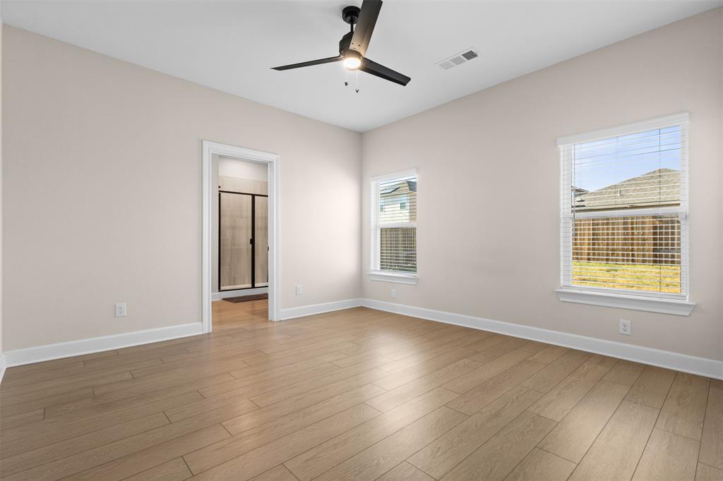Neutral-toned interior featuring wood-finish flooring, a matte black ceiling fan with integrated lighting, and multiple windows with white horizontal blinds