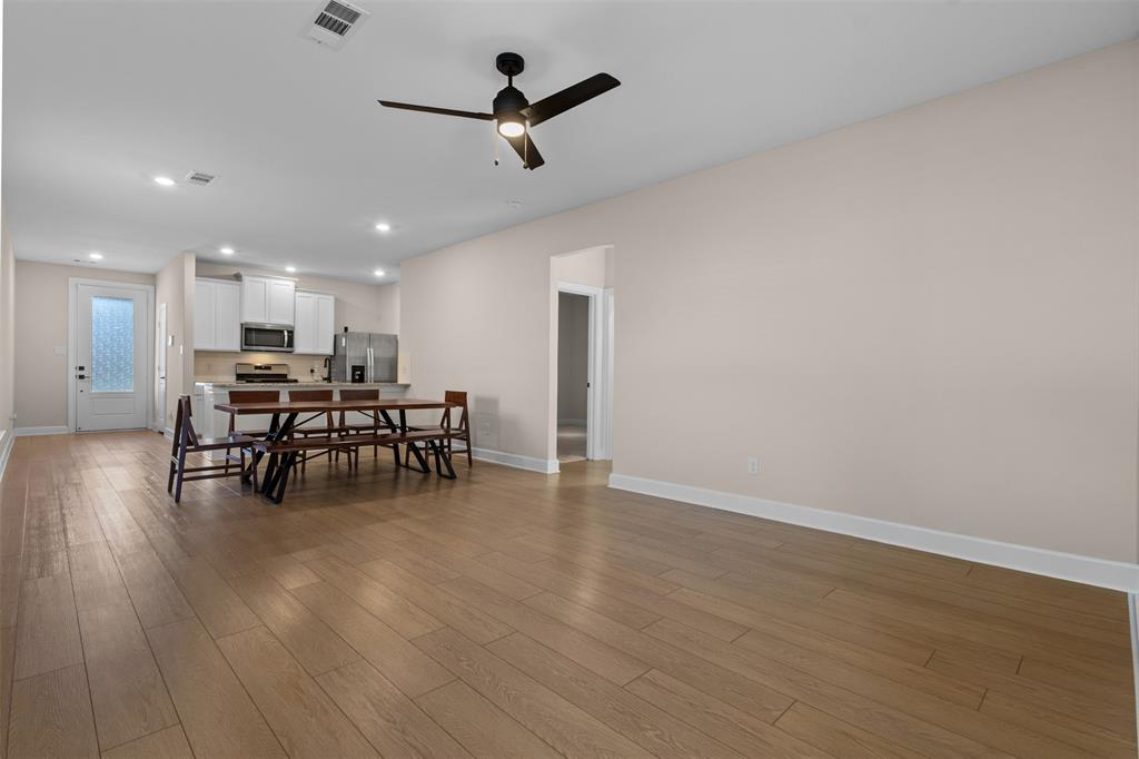 Open-concept interior featuring wood-finish flooring, recessed lighting, a modern ceiling fan, white kitchen cabinetry, and an exterior door with glass detailing
