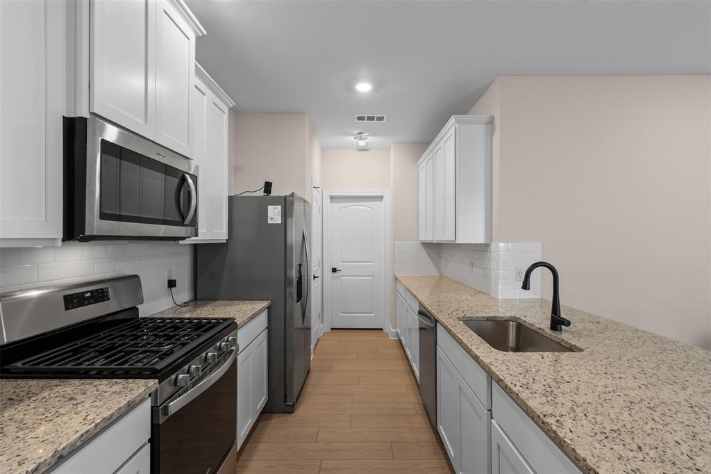 Kitchen featuring white shaker cabinetry, stone-finish countertops, stainless steel appliances, wood-finish flooring, and a subway tile backsplash