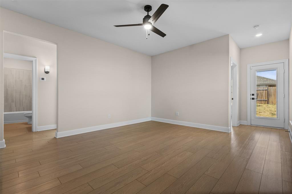 Neutral-toned interior featuring wood-finish flooring, a matte black ceiling fan with integrated lighting, and a glass-paneled exterior door