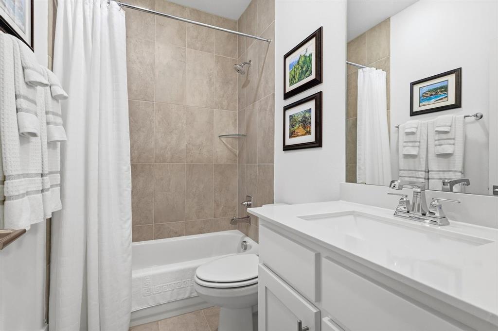 Bathroom featuring a white vanity cabinet with a solid surface countertop, an undermount sink with a polished chrome faucet, a tub-shower combination with floor-to-ceiling tile surround, and a full-width wall mirror