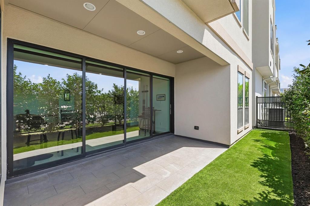 Covered patio with large-format tile flooring, oversized sliding glass doors, recessed lighting, and a fenced yard with artificial turf
