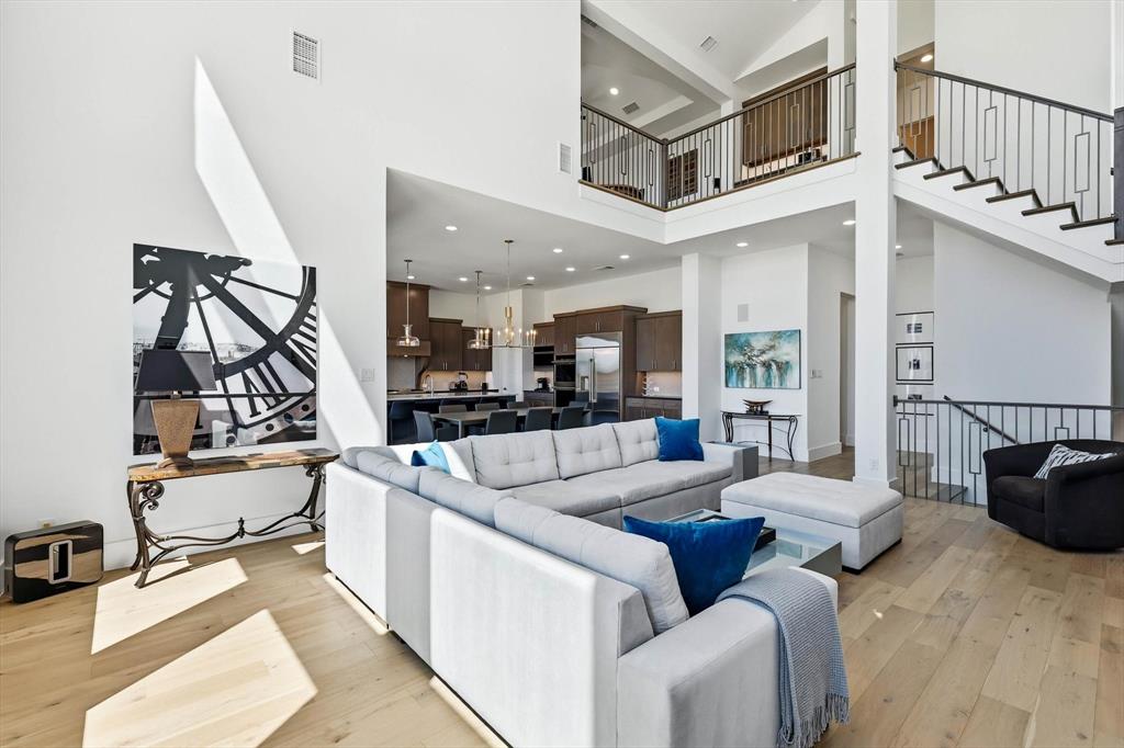 Open-concept floor plan with soaring double-height ceilings, wood-finish flooring, and a staircase featuring wrought iron balusters