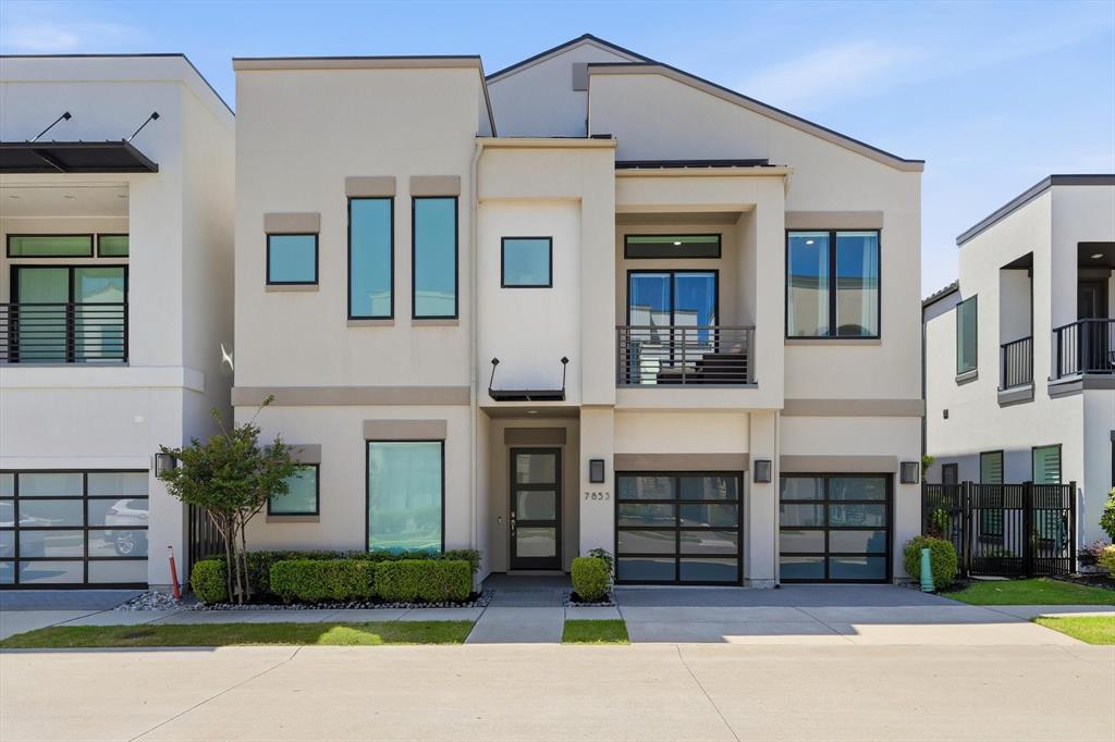 Modern stucco exterior featuring clean architectural lines, a second-story balcony with horizontal metal railing, multiple glass-paneled garage doors, and oversized rectangular windows Modern stucco exterior featuring clean architectural lines, a second-story balcony with horizontal metal railing, multiple glass-paneled garage doors, and oversized rectangular windows