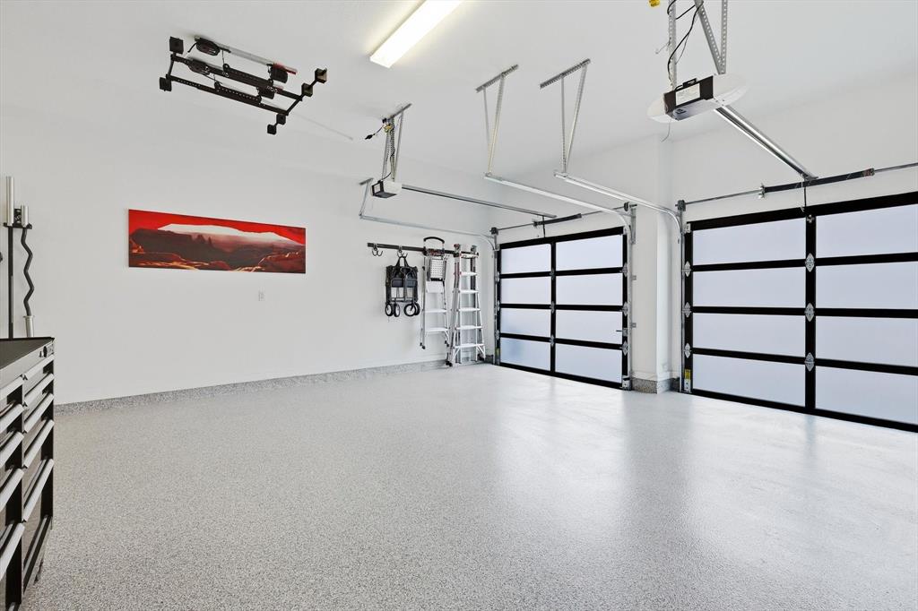Two-car garage featuring frosted glass sectional doors, epoxy-coated flooring, and an automated overhead door opener