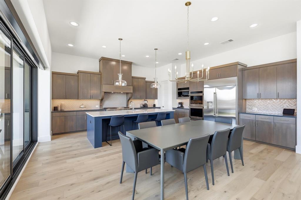 Kitchen featuring wood-finish flooring, two-tone cabinetry with a contrasting island, stone-surfaced countertops, herringbone-patterned tile backsplash, and built-in double wall ovens