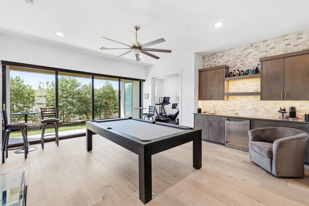 Multi-panel sliding glass doors, wet bar with wood cabinetry and stone backsplash, recessed lighting, and wood-finish flooring Multi-panel sliding glass doors, wet bar with wood cabinetry and stone backsplash, recessed lighting, and wood-finish flooring