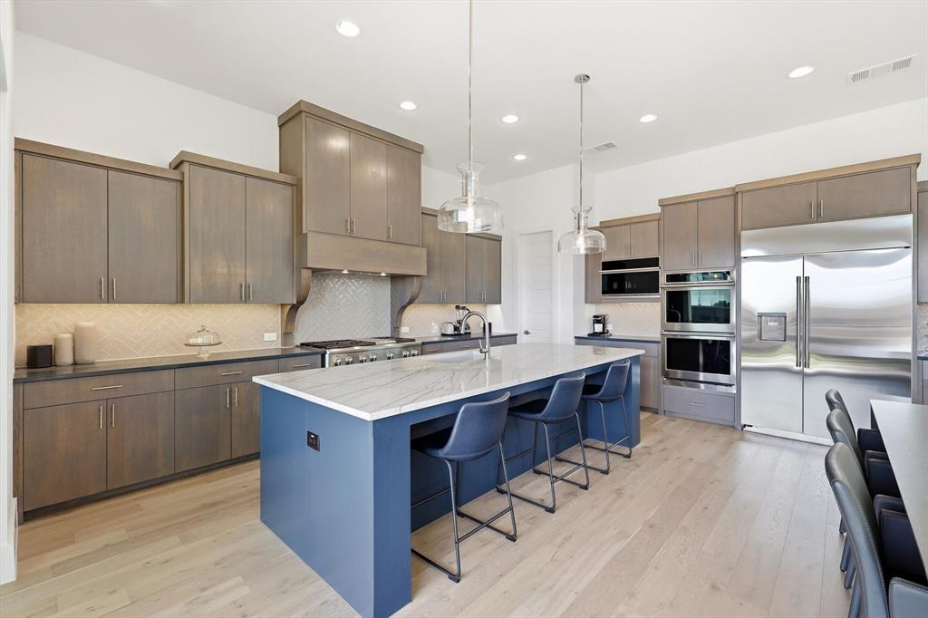 Kitchen featuring custom stained cabinetry, a central island with stone-finish countertops, herringbone tile backsplash, recessed lighting, and stainless steel built-in appliances