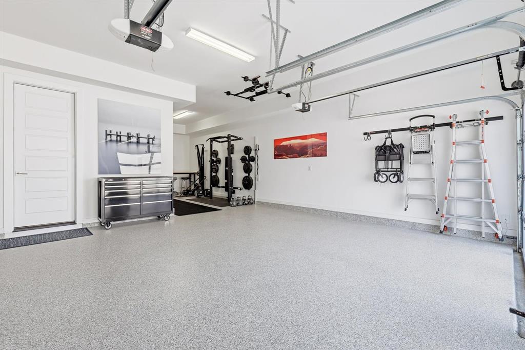 Garage featuring speckled epoxy flooring, white paneled interior door, overhead garage door system, and wall-mounted storage tracks